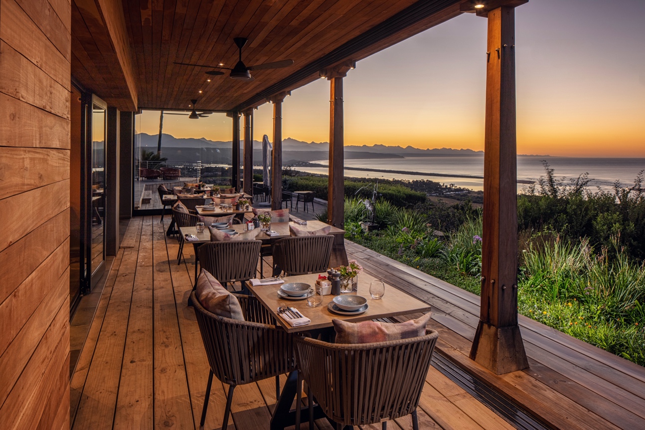 Two wooden ceiling fans under a timber-clad covered patio overlooking the ocean at sunset